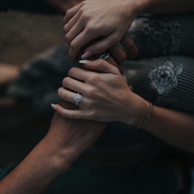 Close-up of two people holding hands intimately, showing a ring.